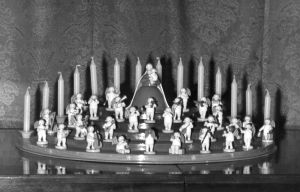 Schwarz-Weiß-Aufnahme vom Engelorchester mit Madonna auf einem Engelberg. Auf den unteren Stufen die Engelmusikanten. An oberster Stelle die Madonna mit Schleier und im langen Kleid. Im Hintergrund Kerzen. 
