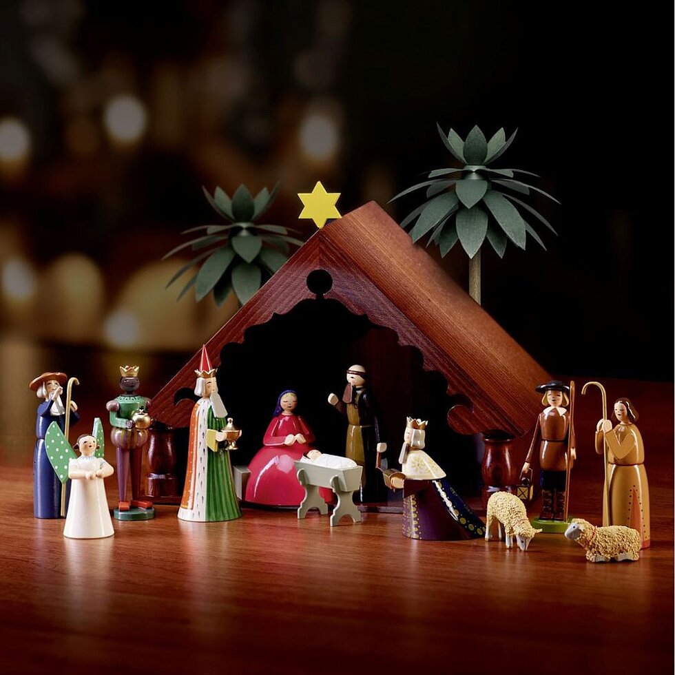 Handgefertigte Weihnachtskrippe von Wendt & Kühn mit Maria, Josef, dem Jesuskind, den Heiligen Drei Königen, Hirten, Schafen und einem Engel vor einem stilisierten Stall.