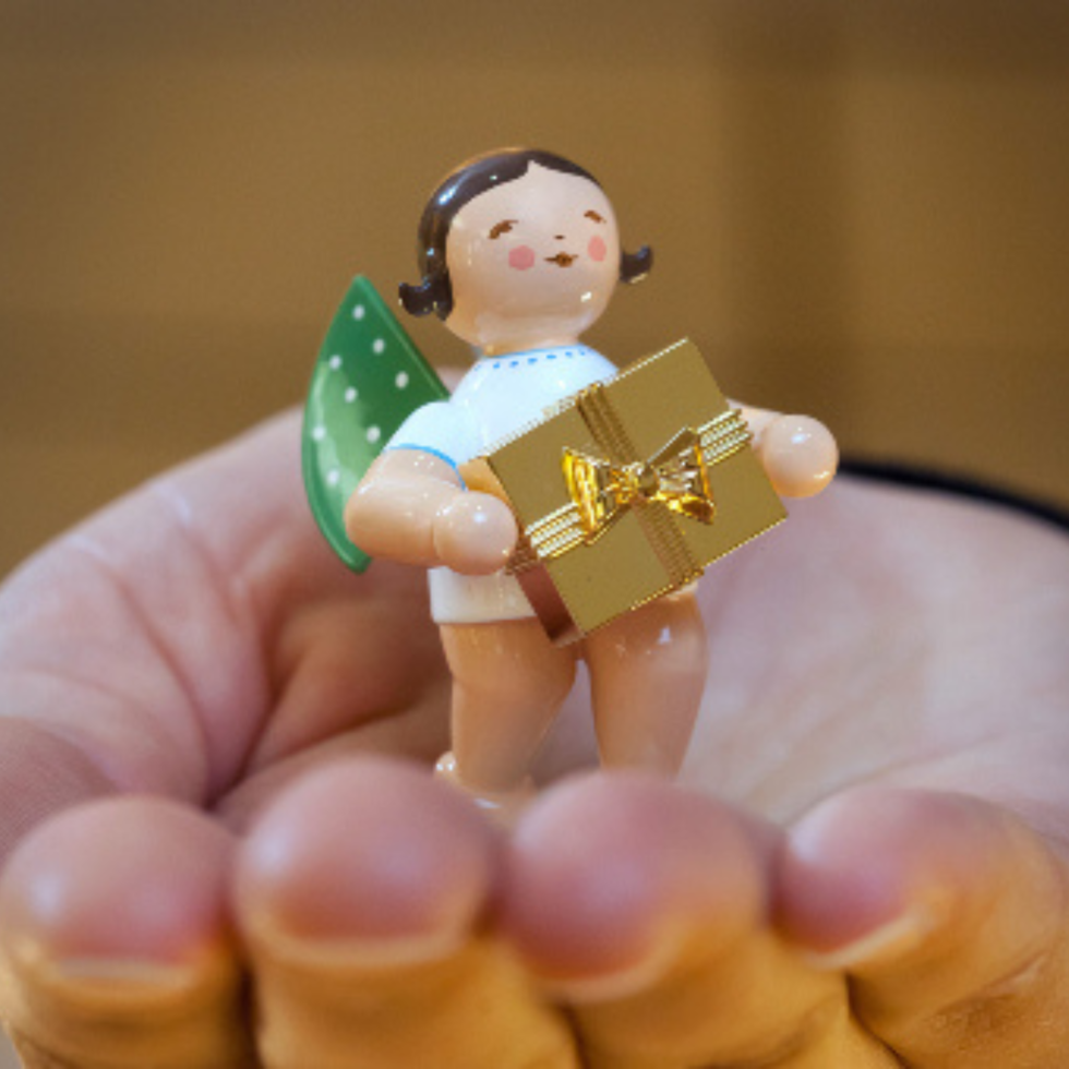 Eine Hand hält einen Elfpunkte-Engel, welcher ein goldenes Geschenk trägt