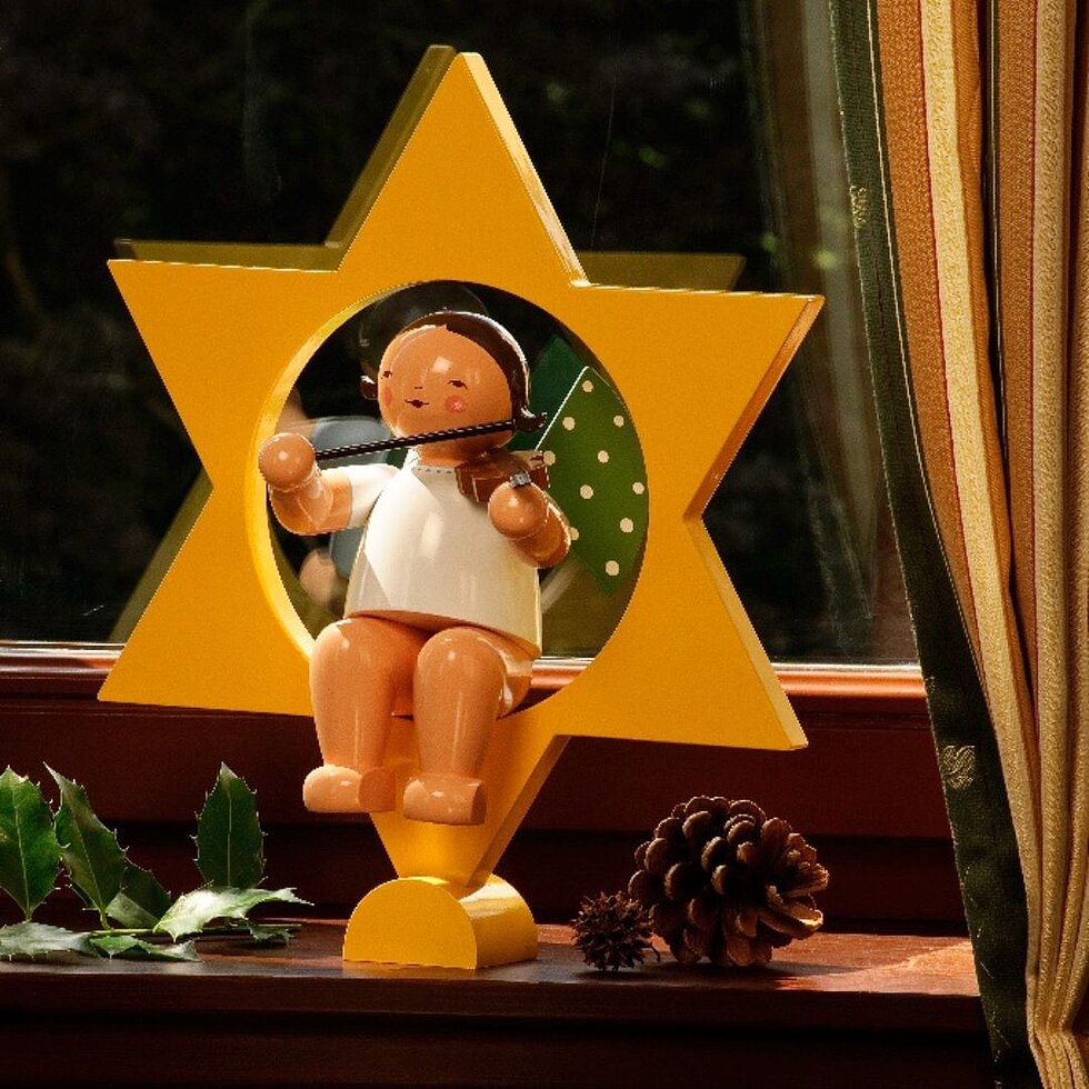 Handgefertigter Engel im Stern von Wendt & Kühn mit Geige als weihnachtliche Fensterdekoration auf einer Fensterbank.