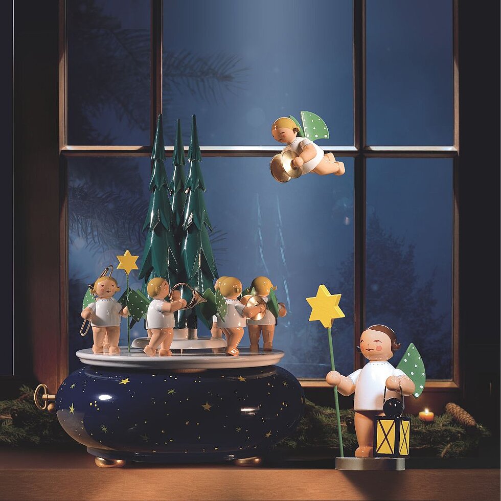 Handgefertigte Spieldose von Wendt & Kühn mit Engelmusikanten unter Tannenbäumen sowie einem Engel mit Laterne und einem schwebenden Engel als festliche Weihnachtsdekoration.