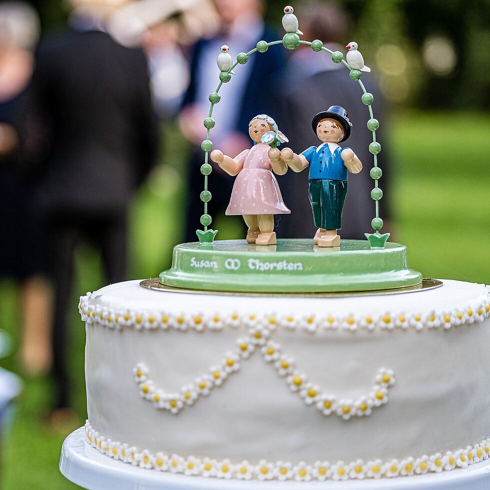 Hochzeitstorte mit einer Tortenfigur eines Liebespaars unter einem grünen Bogen mit weißen Vögeln