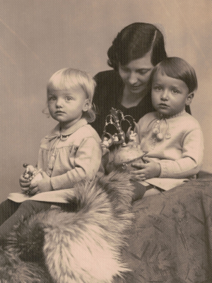 Schwarz-Weiß-Aufnahme. Foto von Olly mit den Kleinkindern Sigrid und Hans. Die drei sitzen auf einem Sessel, über den ein Fell geschlagen wurde. Die Kinder halten jeweils eine Spieldose von Wendt & Kühn in den Händen.