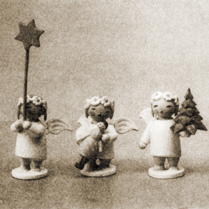 Drei Margeritenengel. Sie halten jeweils einen Stern, ein Bäumchen und eine Puppe. Schwarz-Weiß-Aufnahme.