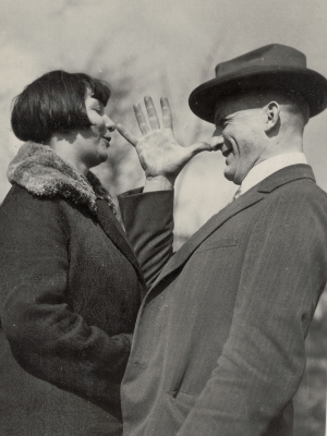 Paar-Foto von Olly und Johannes Wendt im Garten. Beide tragen Mäntel, Johannes außerdem einen Hut. Er zeigt Olly eine "lange Nase".