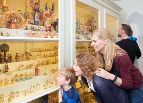 Eine Frau mit zwei Kindern betrachtet begeistert den weißen Musterschrank mit zahlreichen kleinen Figuren in der Ausstellung
