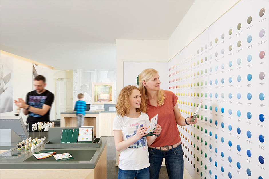 Eine Familie besichtigt die Farbenübersicht, welche an einer Wand angebracht ist. 