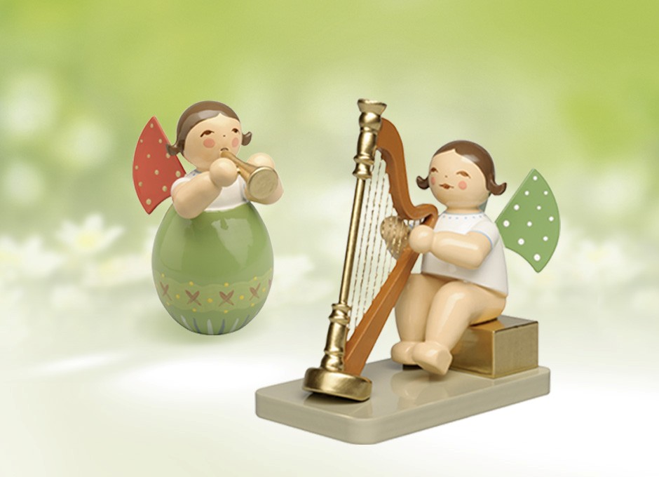 Zwei Holzengel mit grünen Flügeln, einer steht in einem Osterei und spielt Trompete, der andere sitzt an einer Harfe