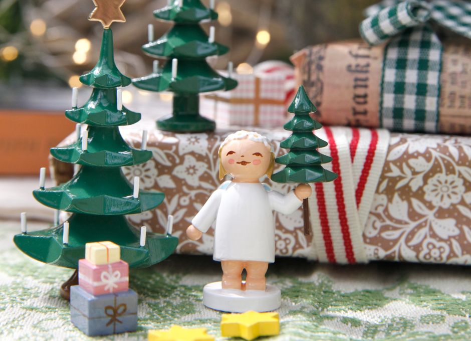 Margeritenengel mit Tannenbaum in der Hand vor Geschenkehaufen